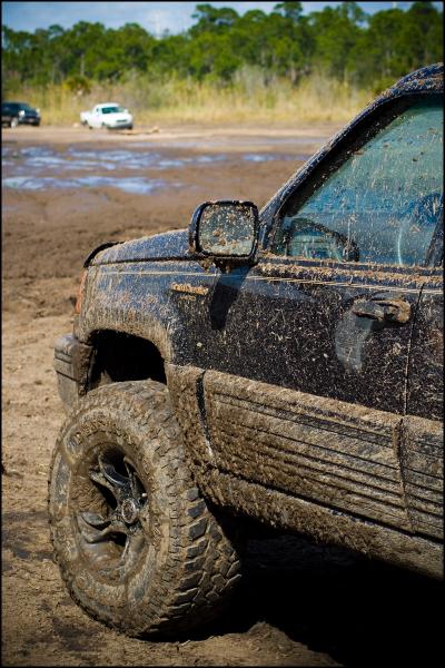 1996 Ford F-150 - A Jeep Grand Cherokee is covered in mud after driving through a muddy area, with other vehicles visible in the distance.