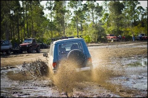 1996 Ford F-150 - An off-road vehicle navigates a muddy track, kicking up a large spray of dirt and water.