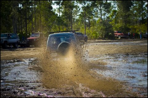 1996 Ford F-150 - Multiple off-road vehicles navigate a challenging muddy terrain, creating significant splashes.