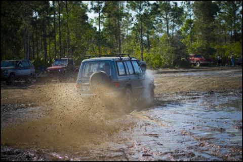 1996 Ford F-150 - Several off-road vehicles are navigating a muddy track, kicking up large splashes of water and dirt.
