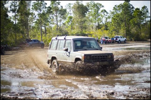 1996 Ford F-150 - An off-road SUV navigates a muddy terrain, kicking up water and dirt.
