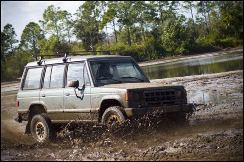 1996 Ford F-150 - An SUV navigates a muddy terrain, kicking up water and dirt as it drives through the mire.