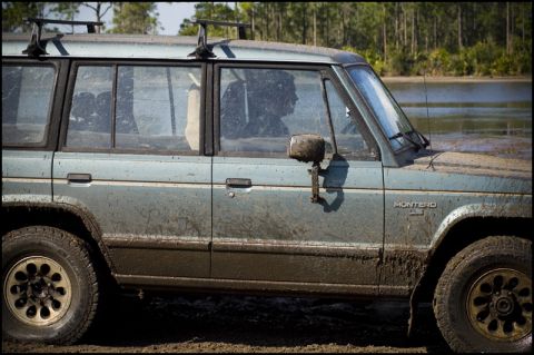 1996 Ford F-150 - Muddy Mitsubishi Montero off-roading near water, side profile visible.