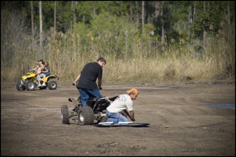 1996 Ford F-150 - People ride ATVs in a dirt area with trees and tall grass. One ATV carries three people, while another has two people.