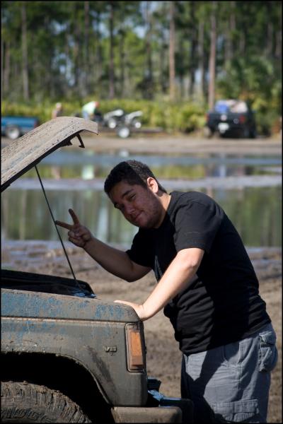 1996 Ford F-150 - A man stands by the open hood of a dirty truck, making a peace sign with his hand. Other vehicles are visible in the background.