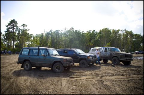 1996 Ford F-150 - A muddy 1996 Ford F-150 is parked with other off-road vehicles under a bright sky.