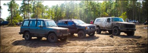 1996 Ford F-150 - Three off-road SUVs are parked in a dirt lot with a wooded area behind them.