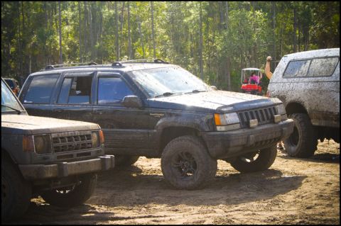 1996 Ford F-150 - A muddy black Jeep Grand Cherokee is parked on a dirt track with other vehicles nearby.