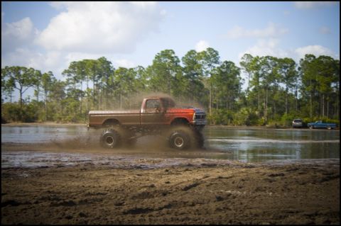 1996 Ford F-150 - A modified pickup truck with oversized tires navigates a muddy terrain, creating a large splash.