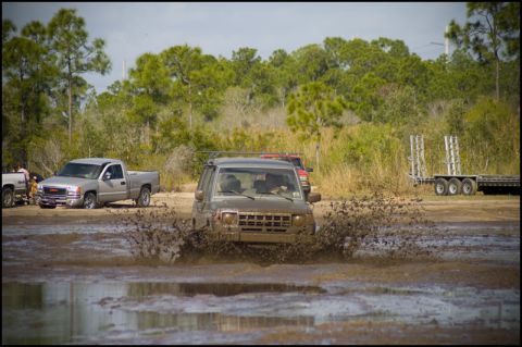 1996 Ford F-150 - An SUV navigates a muddy obstacle course, kicking up a large spray of water and mud.