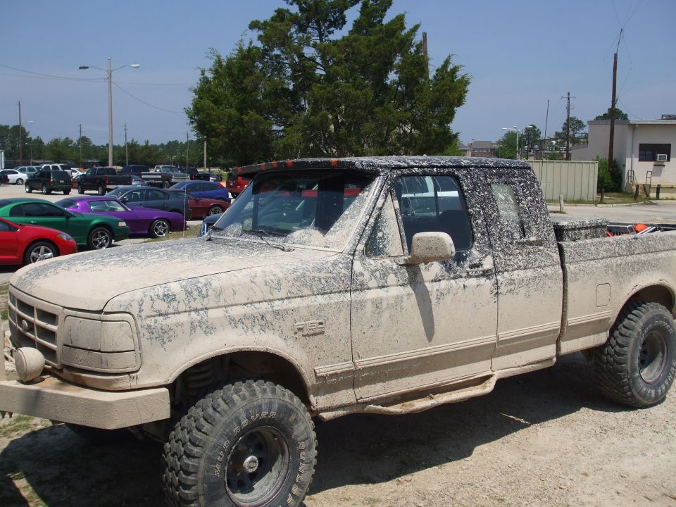 Mud-covered lifted Ford F-150 extended cab pickup on Mud Rover tires in a gravel lot