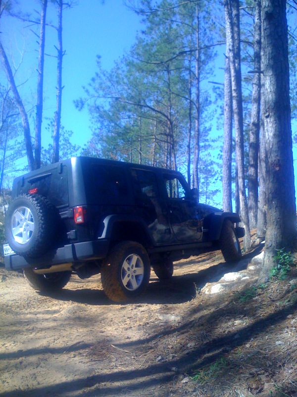 Black Jeep Wrangler on a dirt trail, rear spare tire visible, side view