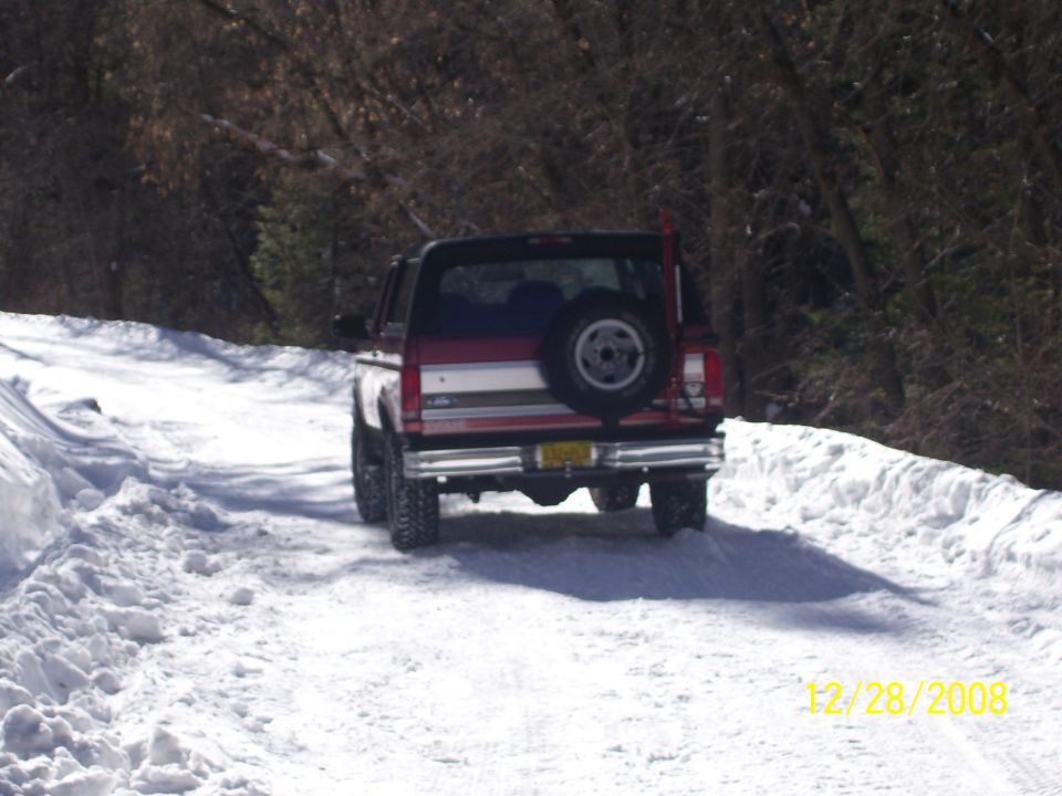 Red and white Ford Bronco with a spare tire on the back, driving on a snow-covered road