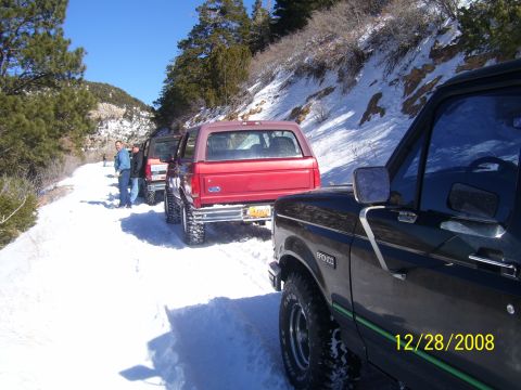1993 Ford Bronco - A convoy of Ford Broncos navigates a snowy mountain road on a clear winter day.