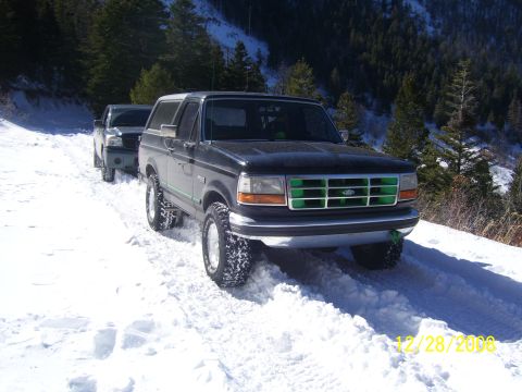 1993 Ford Bronco - A 1993 Ford Bronco navigates a snowy mountain road, with another vehicle following behind.
