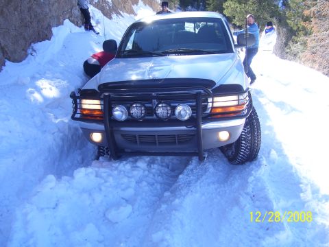 1993 Ford Bronco - A Dodge Dakota pickup truck is stuck in the snow on a rural road, with people attempting to free it.