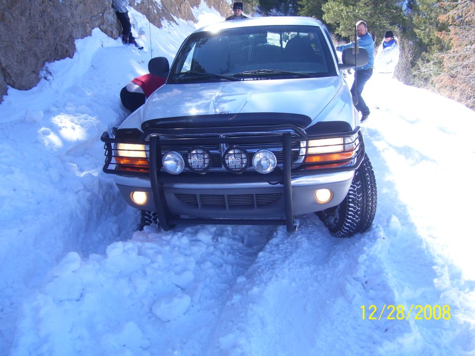Silver Dodge Dakota pickup truck with a bull bar and auxiliary lights stuck in deep snow