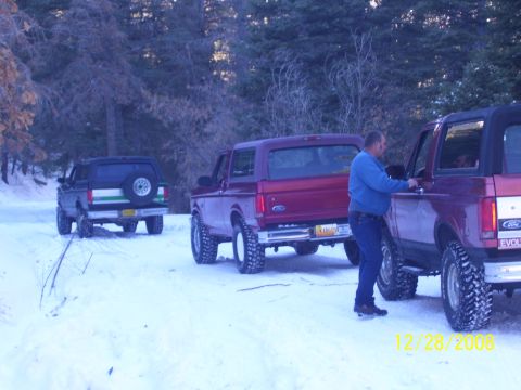 1993 Ford Bronco - Three Ford Broncos are parked on a snow-covered trail surrounded by trees, with one person interacting with a vehicle.