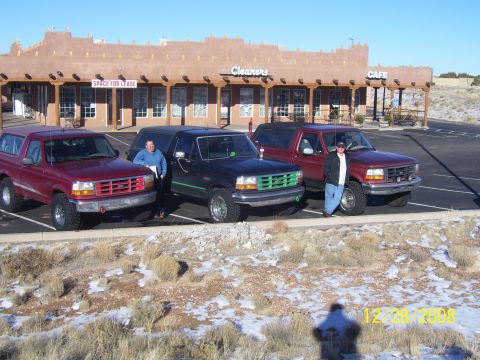 1993 Ford Bronco - Three 1993 Ford Broncos parked in front of a strip mall with 'Cleaners' and 'Cafe' signs. Two men are standing with the vehicles.
