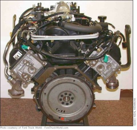 2007 Ford Mustang - A V8 engine is shown with its complex network of hoses and wiring, and a prominent flywheel.