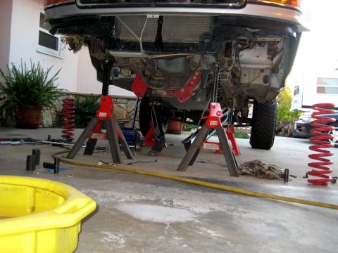 1996 Ford Bronco - The front suspension of a vehicle is disassembled and supported by jack stands, with tools and parts scattered around.