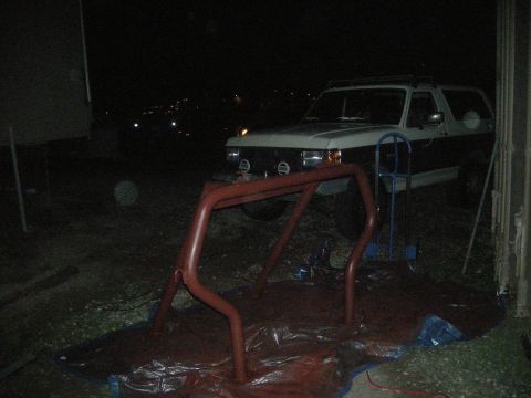 1991 Ford Bronco - A two-tone Ford Bronco from the late 1980s is parked outdoors at night, with a red roll cage in front of it.