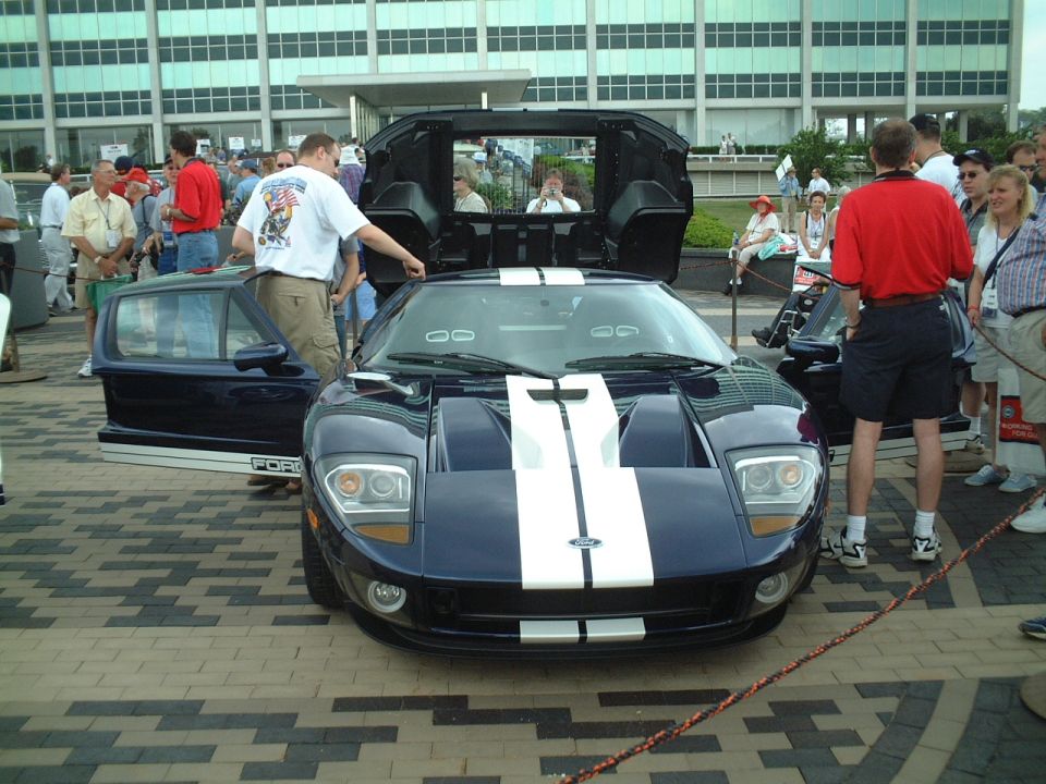 Dark blue Ford GT with white stripes, doors open, at outdoor car show
