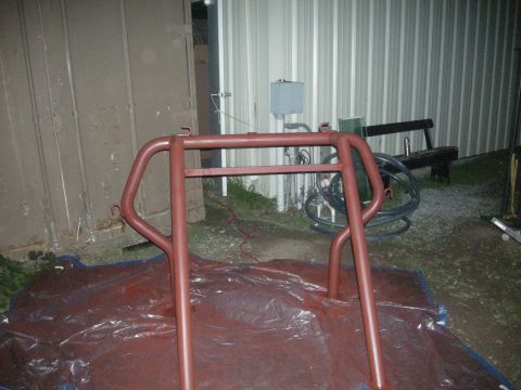 1991 Ford Bronco - A red roll cage is set up on a plastic tarp, with a building and some outdoor items in the background.