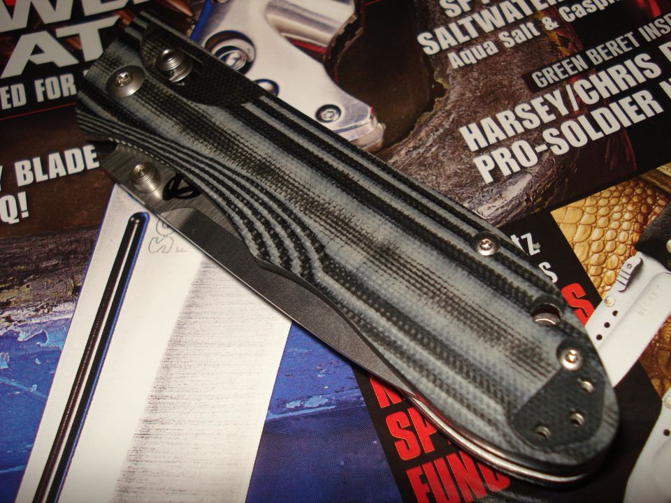 Knife with gray and black striped handle, silver blade, and visible screws, resting on magazines