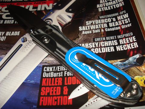 2000 Ford Crown Victoria - A knife is shown with a blue sticker and clip, placed on top of magazines that feature knife-related content.