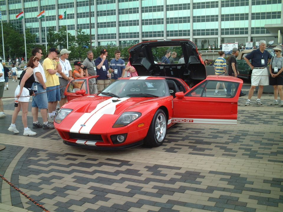 Red Ford GT with white stripes, doors and rear open, at an outdoor car show with onlookers