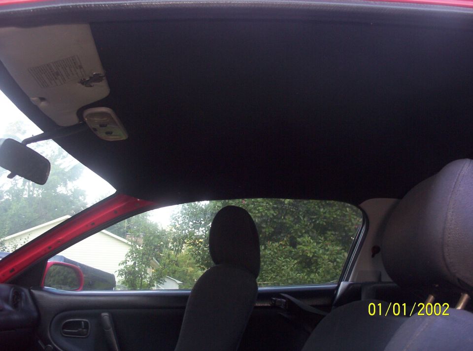 Interior of a red car showing black headliner, sun visor, and driver's seat.