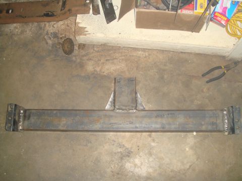 1992 Ford Bronco - A fabricated steel crossmember, likely for a vehicle frame, is shown lying on a concrete floor. The crossmember has a central triangular su…