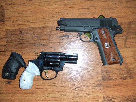 1996 Ford Bronco - Two handguns are displayed on a wooden surface. One is a black revolver with white grips and a gold trigger. The other is a dark grey semi-…
