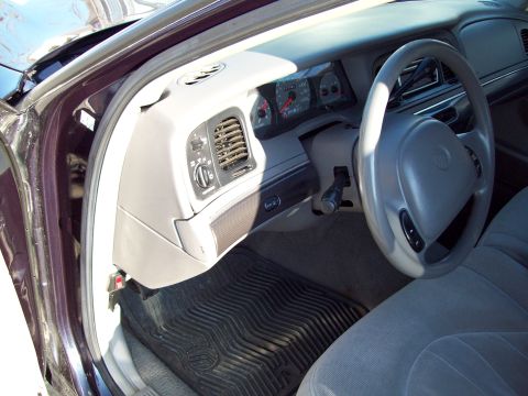 1999 Mercury Grand Marquis - Driver's side interior of a gray-trimmed Mercury sedan viewed through the open door, showing the four-spoke steering wheel with Mercury emb…