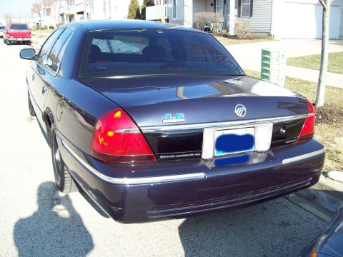 1999 Mercury Grand Marquis - Driver-side rear three-quarter view of a dark blue Mercury Grand Marquis GS parked at a suburban curb, with the license plate digitally bla…