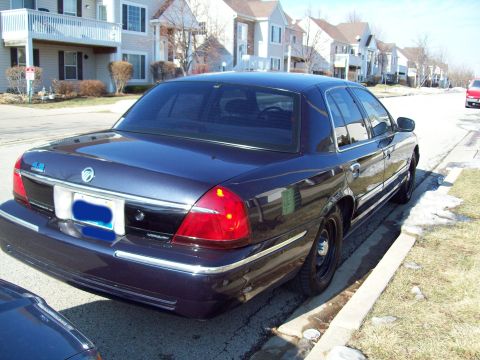 1999 Mercury Grand Marquis - The rear passenger side of a dark blue sedan is parked on a residential street next to a curb. The car has tinted windows and chrome trim a…