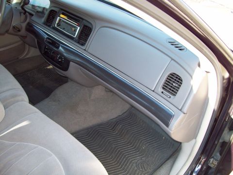 1999 Mercury Grand Marquis - Interior shot through the open passenger door of a gray cloth-trimmed sedan, showing the dashboard with a carbon-fiber-look trim strip runn…