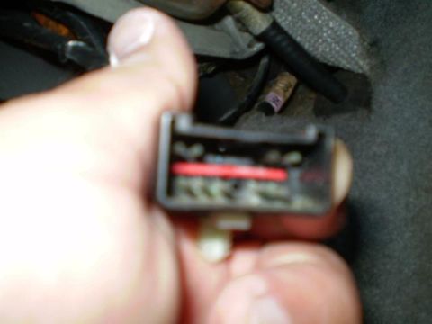 1996 Ford Bronco - A hand holds a black electrical connector with a red wire visible inside. The connector appears to be part of a vehicle's wiring harness.