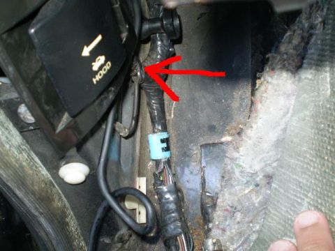 1996 Ford Bronco - A close-up view of a black plastic component with a yellow arrow and the word "HOOD" printed on it, with wiring bundles and a red arrow poi…