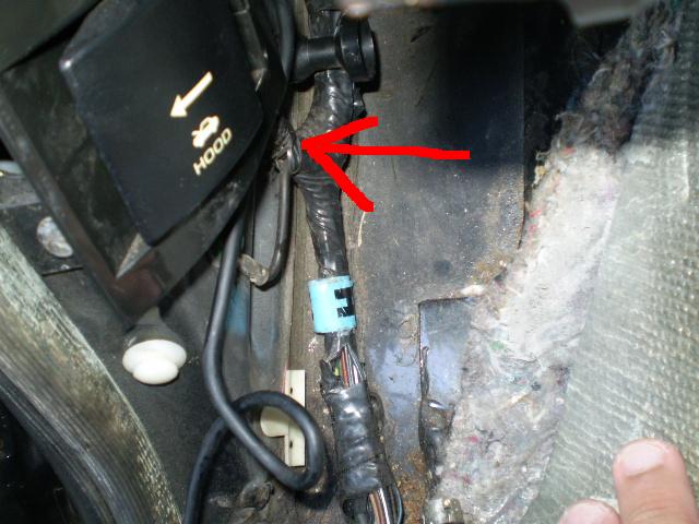 Black plastic hood release lever with yellow text and arrow, connected to wiring.