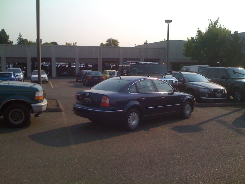 Dark blue VW Passat sedan parked in a busy lot, rear three-quarter view