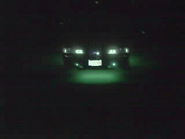 Dark sedan at night, front view, headlights on with green glow under the front bumper