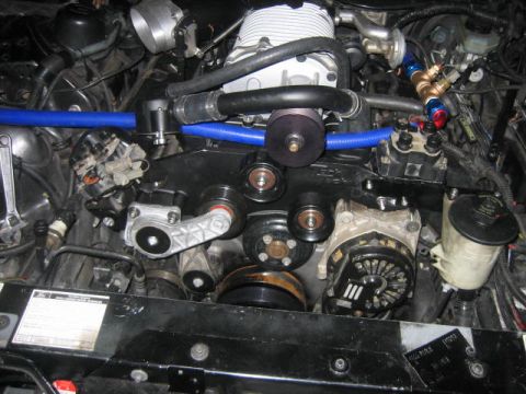 1996 Ford Thunderbird - A close-up view of a modified engine bay, featuring a supercharger, blue hoses, and various pulleys and belts. The engine components are bl…