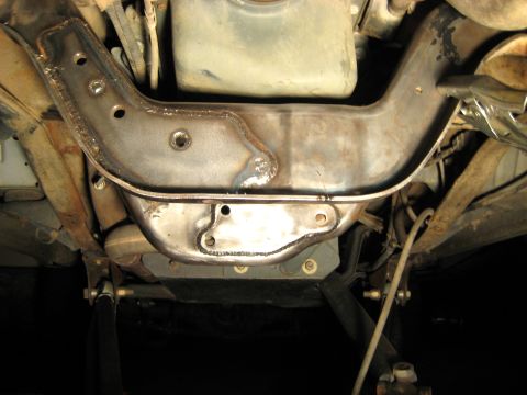 1996 Ford Bronco - The underside of a vehicle shows a heavily modified, dark metal crossmember that has been welded and reinforced. The vehicle is supported b…