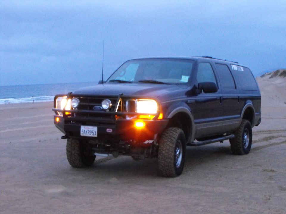 Dark blue Ford Excursion SUV on a beach with a custom bumper and lights.