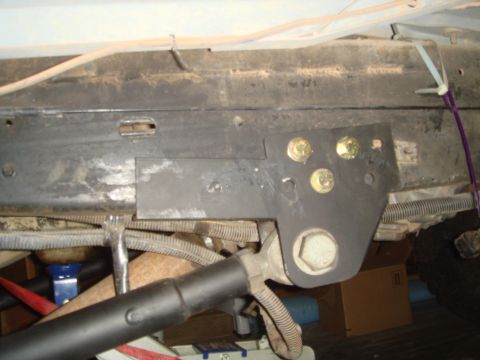 1992 Ford Bronco - A black metal bracket with multiple bolts is attached to the underside of a vehicle frame. Wiring harnesses and other components are visibl…