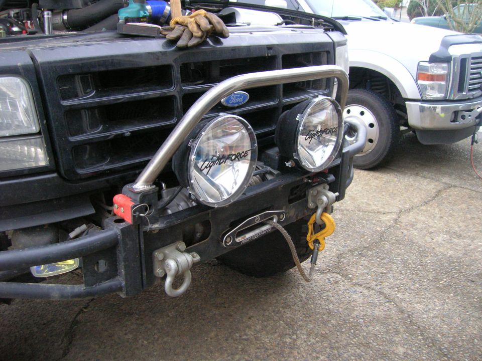 Modified black Ford Bronco bumper with auxiliary lights, winch, and tow hook.