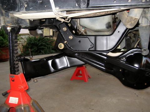 1996 Ford Bronco - A black suspension component, likely a control arm or bracket, is installed on the underside of a vehicle. The vehicle is supported by red…