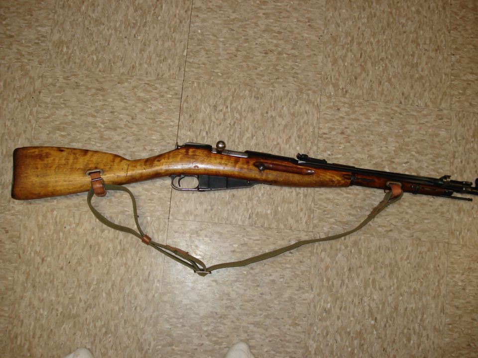 A Mosin-Nagant rifle with a sling on a tiled floor.